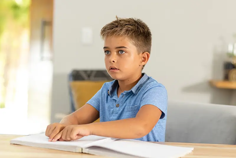 A young student sitting at a desk reading a braille book